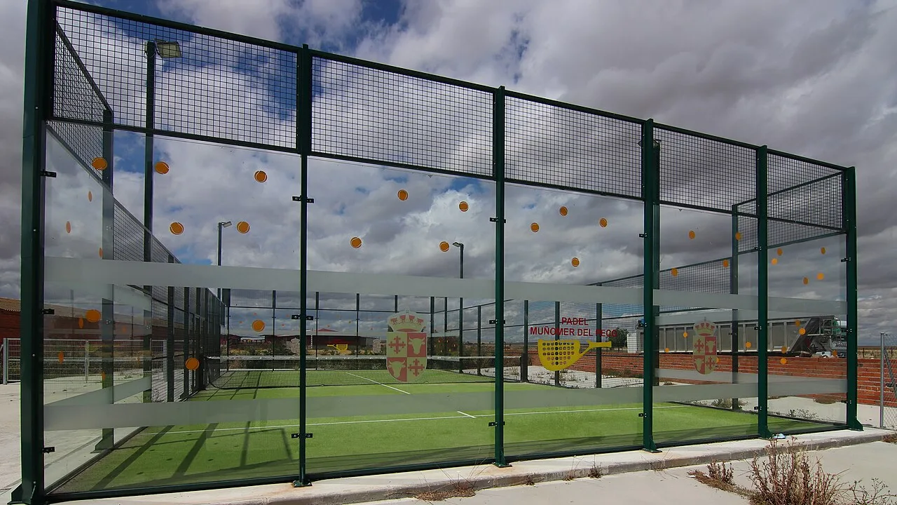 An outdoor padel court enclosed by glass walls and green mesh fencing