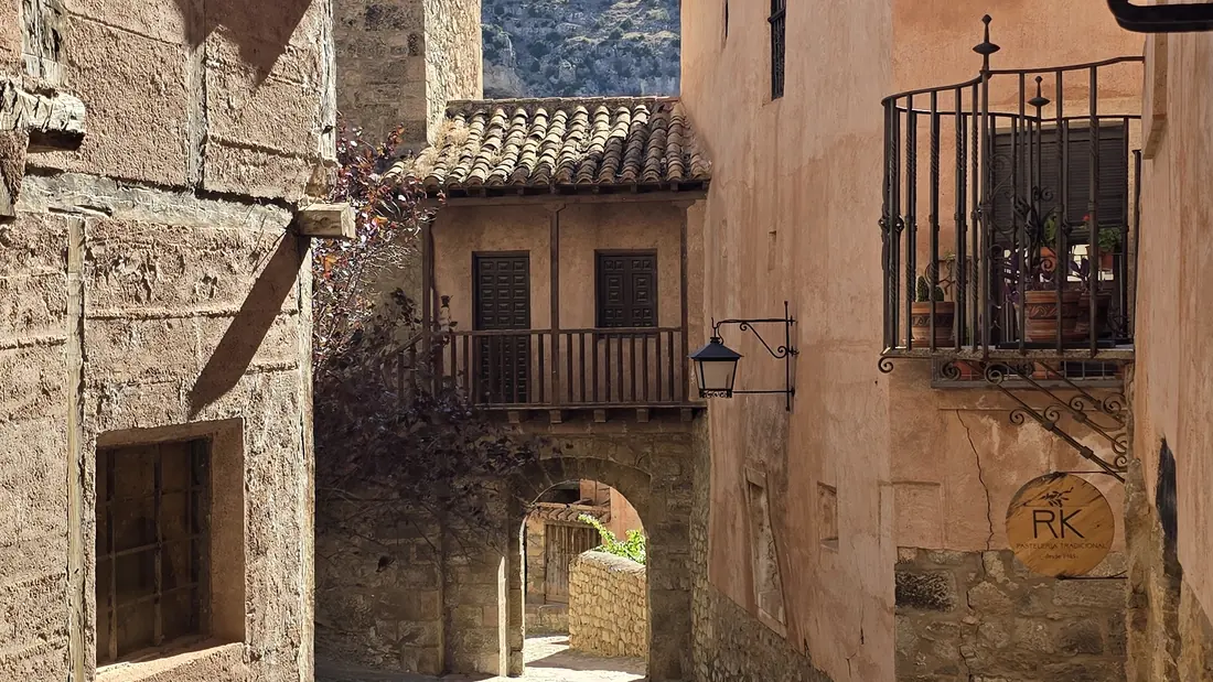 Una calle empedrada y estrecha de Albarracín que lleva a un arco de piedra, entre casas ocres con balcones de forja