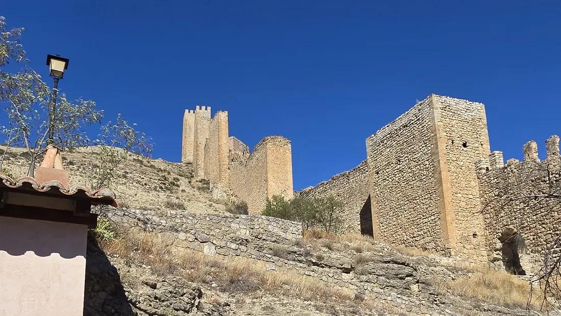 Las murallas medievales y las torres cuadradas de Albarracín sobre la cresta rocosa encima de la ciudad, bajo un cielo azul intenso