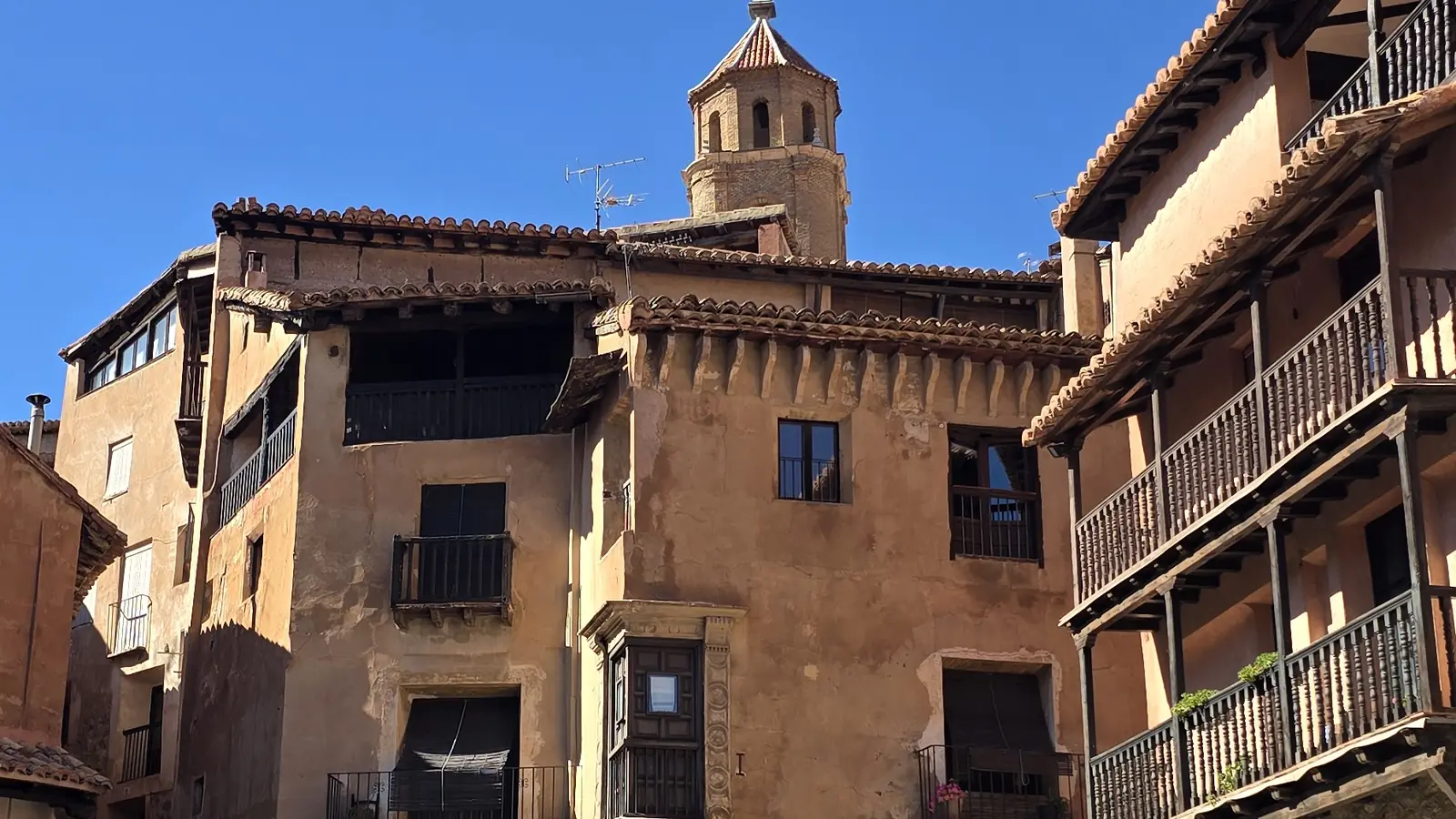 Casas de piedra ocre con balcones de madera alrededor de una plaza de Albarracín, con un campanario sobre los tejados