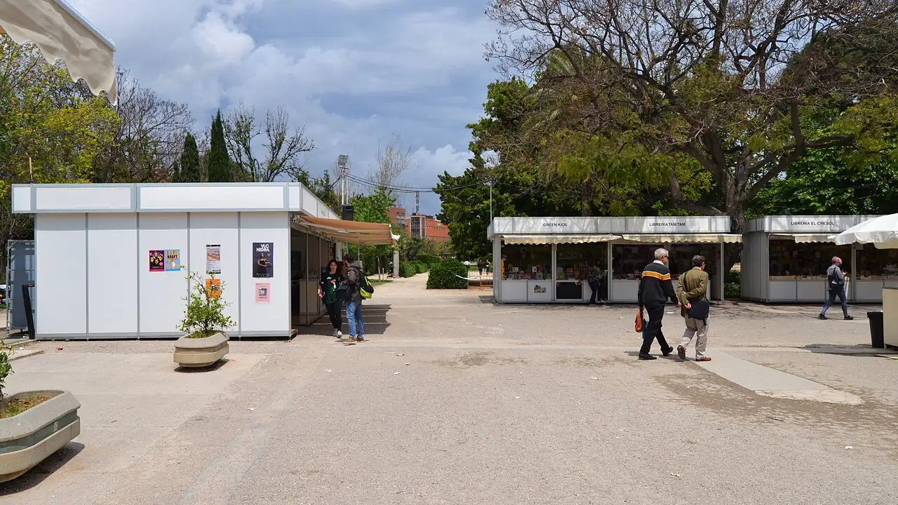 Book stalls under the trees of the Jardins de Vivers in Valencia during the Fira del Llibre, visitors browsing along the path