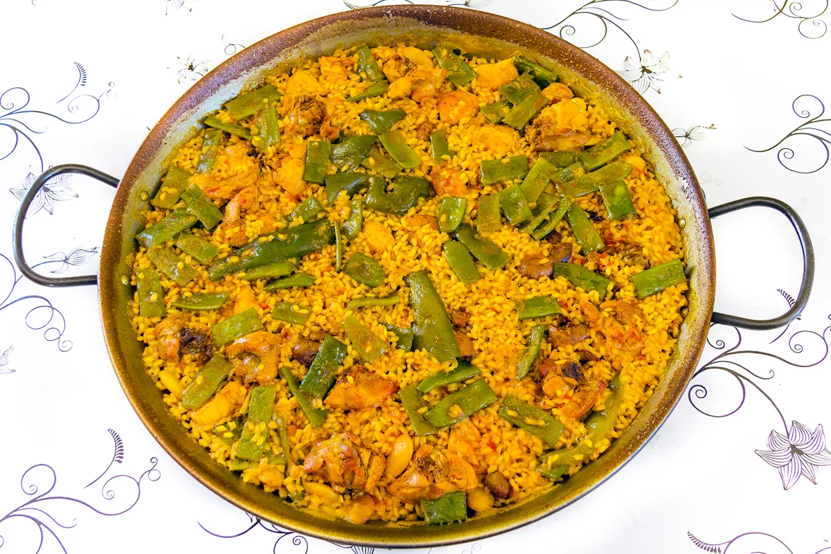 Una paella valenciana auténtica con pollo y judía plana en una paellera tradicional