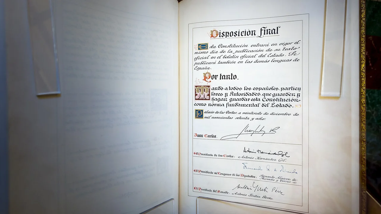 An open bound volume showing the final provision of the Spanish Constitution, hand-lettered and signed by King Juan Carlos I and the presidents of the Cortes, the Congreso and the Senado