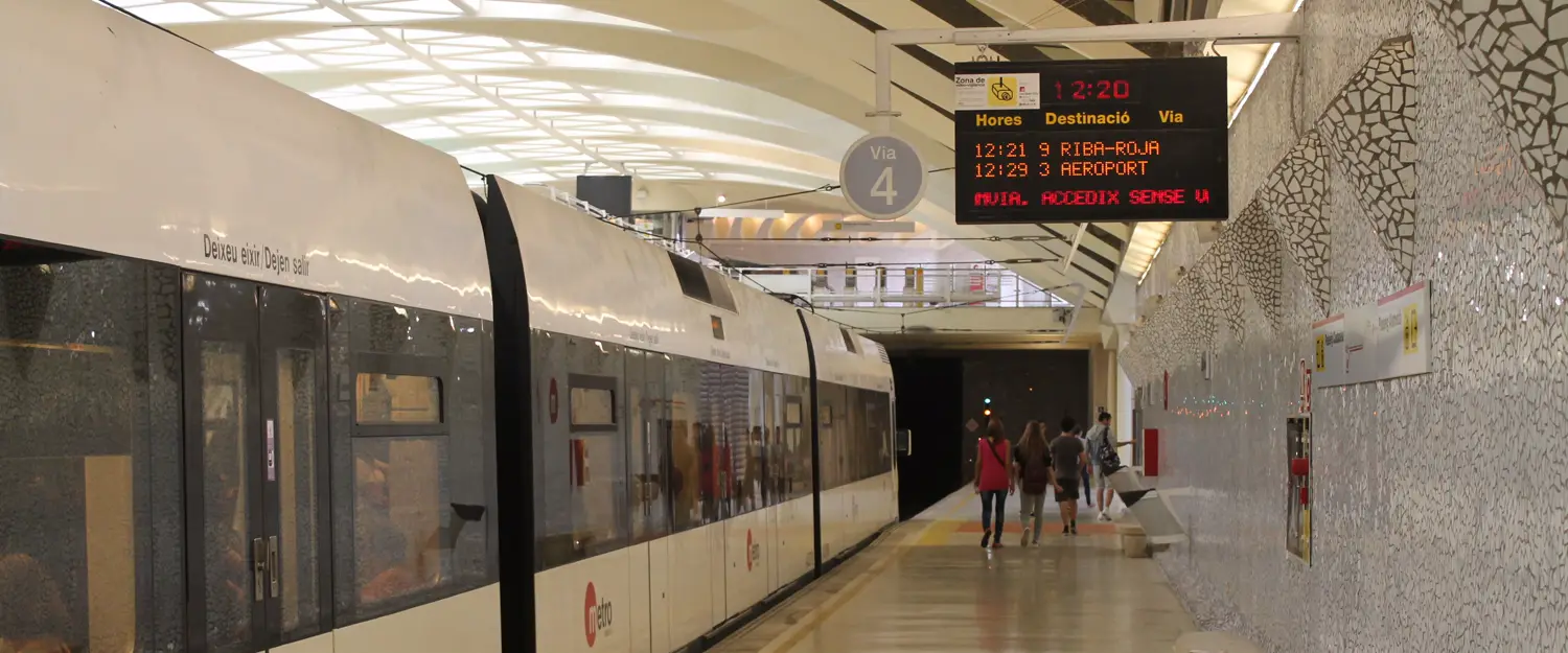 A Metrovalencia train waiting at the underground platform of Alameda station, with the departures board lit up overhead