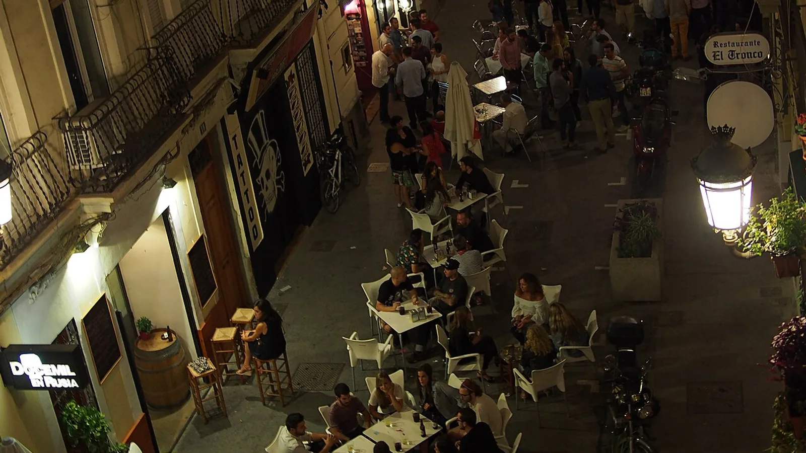 A pedestrianised street in the Ruzafa neighbourhood at night, lantern-lit balconies above and terrace tables crowded with people