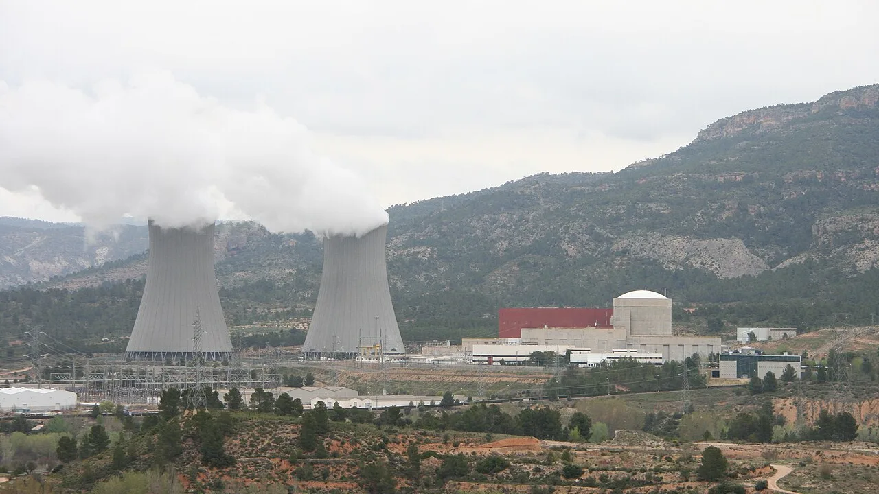A nuclear power station with two steaming cooling towers set in a dry pine covered valley, switchyard and pylons in the foreground
