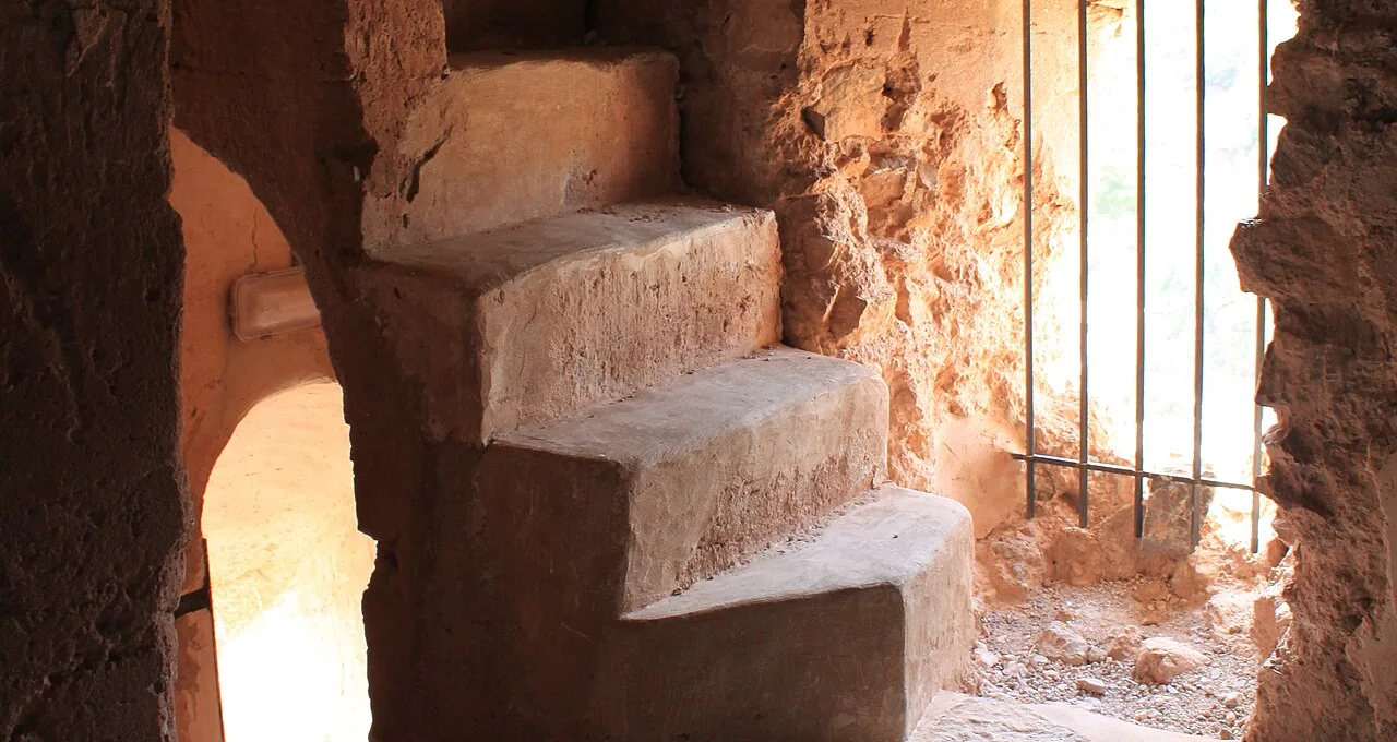 Uitgesleten stenen treden die binnen in de toren van het kasteel van Beselga omhoog draaien, verlicht door een venster met tralies