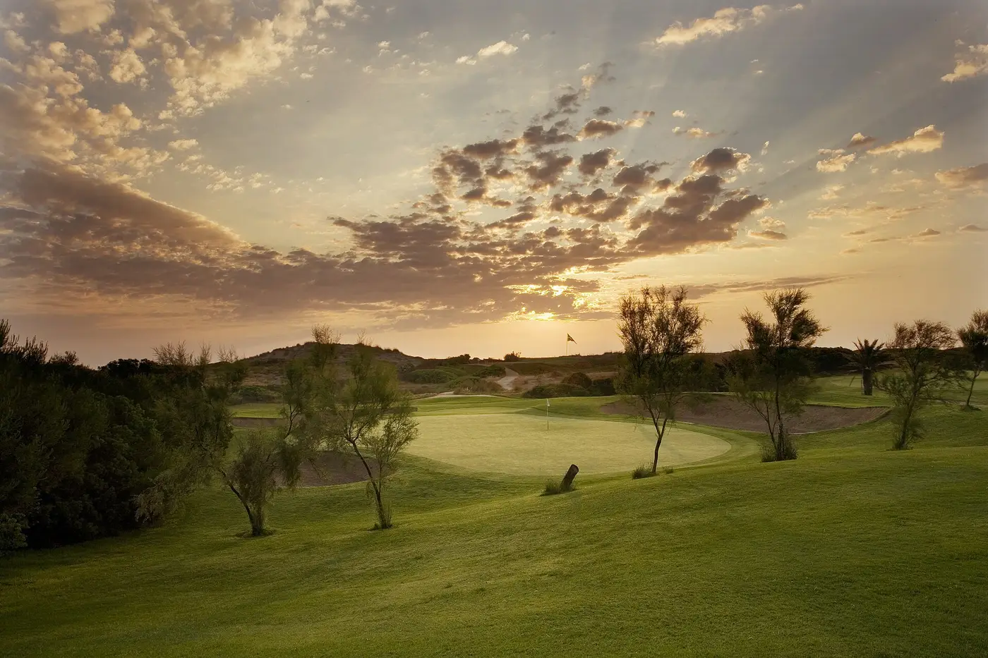 Un green du golf d'El Saler avec des dunes et des arbres en arrière-plan au coucher du soleil, dans le parc naturel de l'Albufera au sud de Valencia