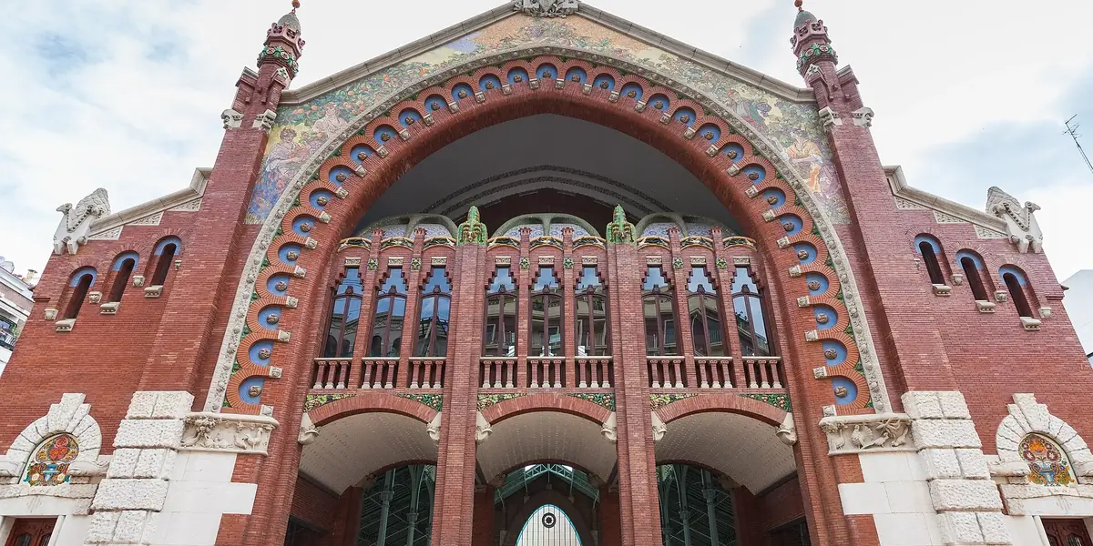 De modernistische gevel van rode baksteen van de Mercado de Colón in Valencia, met de grote boog, keramische versiering en hoge pinakels