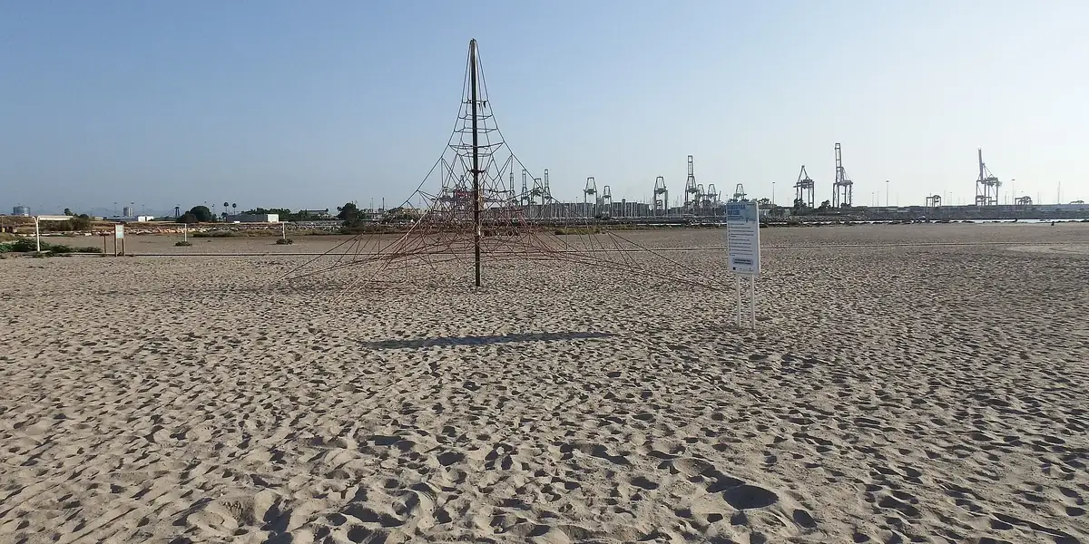 Breed zandstrand bij Pinedo met een klimrek van touw en de kranen van de haven van Valencia aan de horizon