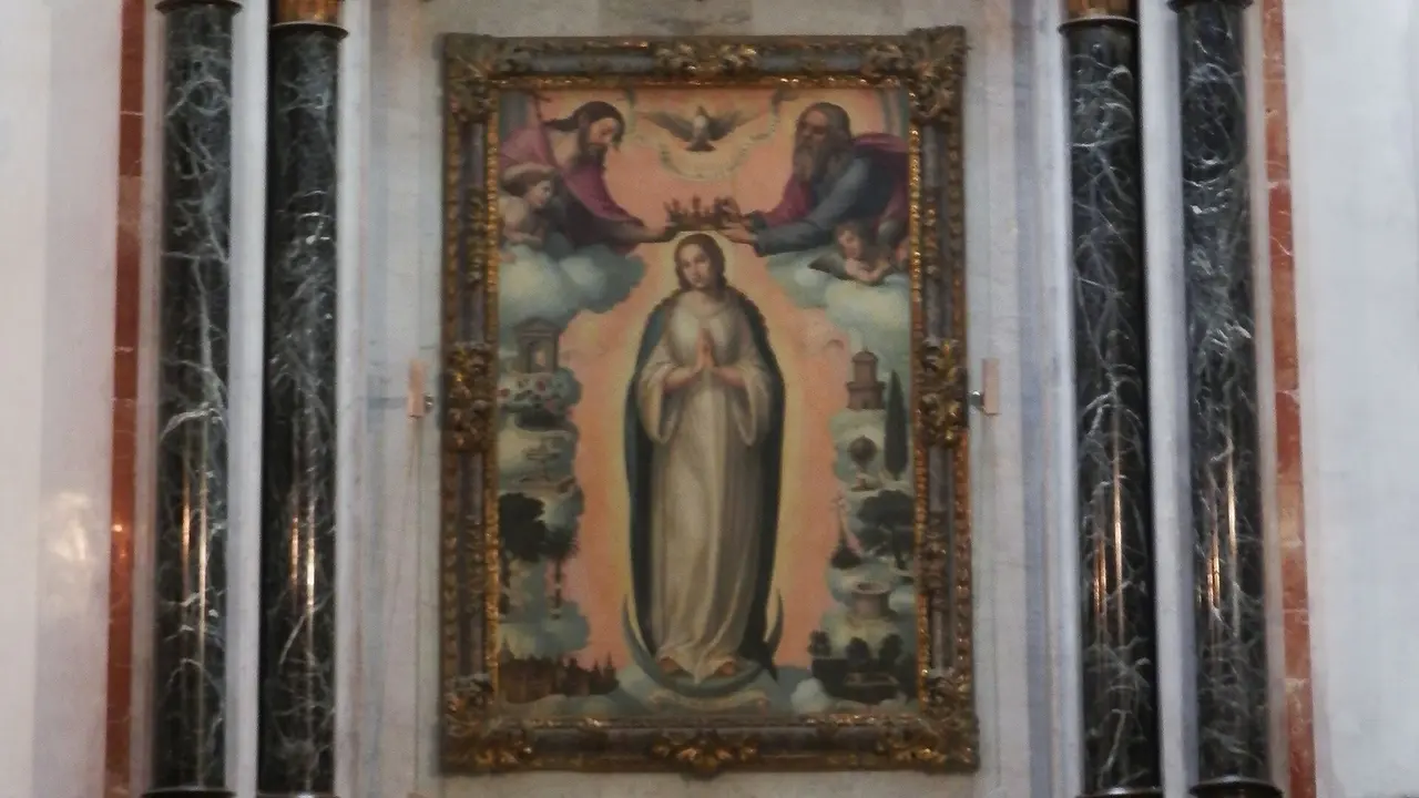 Une peinture de la Renaissance dans un retable de marbre : Marie se tient sur un croissant de lune, les mains jointes, tandis que le Christ et Dieu le Père tiennent une couronne au-dessus de sa tête, avec une tour, un puits et des jardins de chaque côté