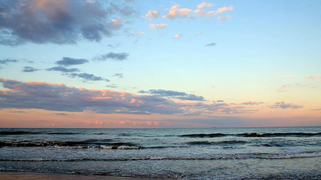 De zee bij de Platja del Cabanyal in Valencia in de schemering, kleine golven onder een roze en blauwe lucht, het strand waar de vuren van Sant Joan worden aangestoken
