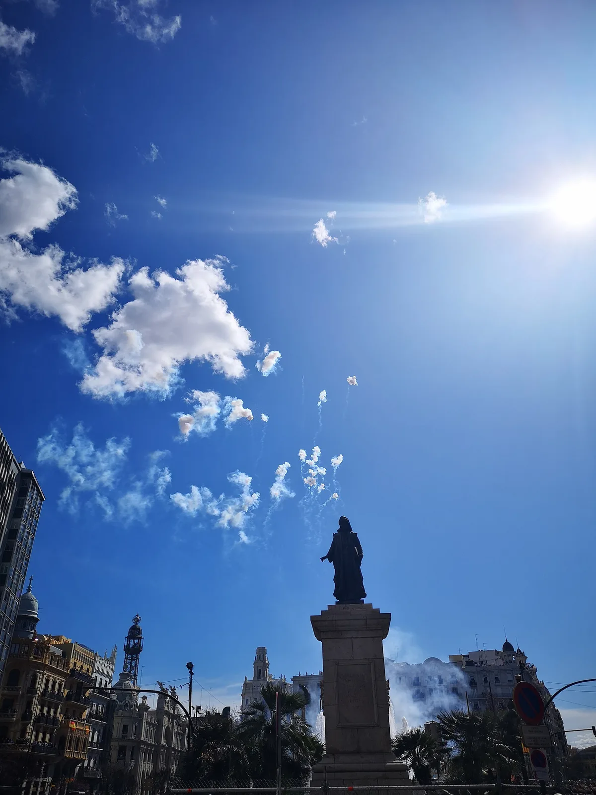 A mascleta firing in Plaza del Ayuntamiento, smoke rising past a statue