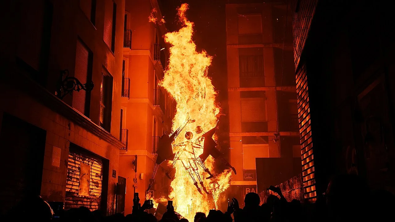 Un monumento fallero ardiendo en una calle estrecha de Valencia durante la cremà, con la multitud recortada contra las llamas
