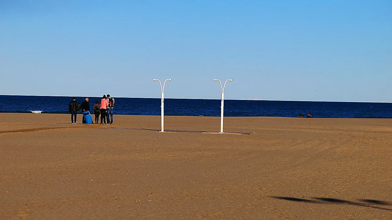 The wide sand of the Platja del Cabanyal in Valencia on a clear day in late spring, a few people at the water's edge and the sea a deep blue