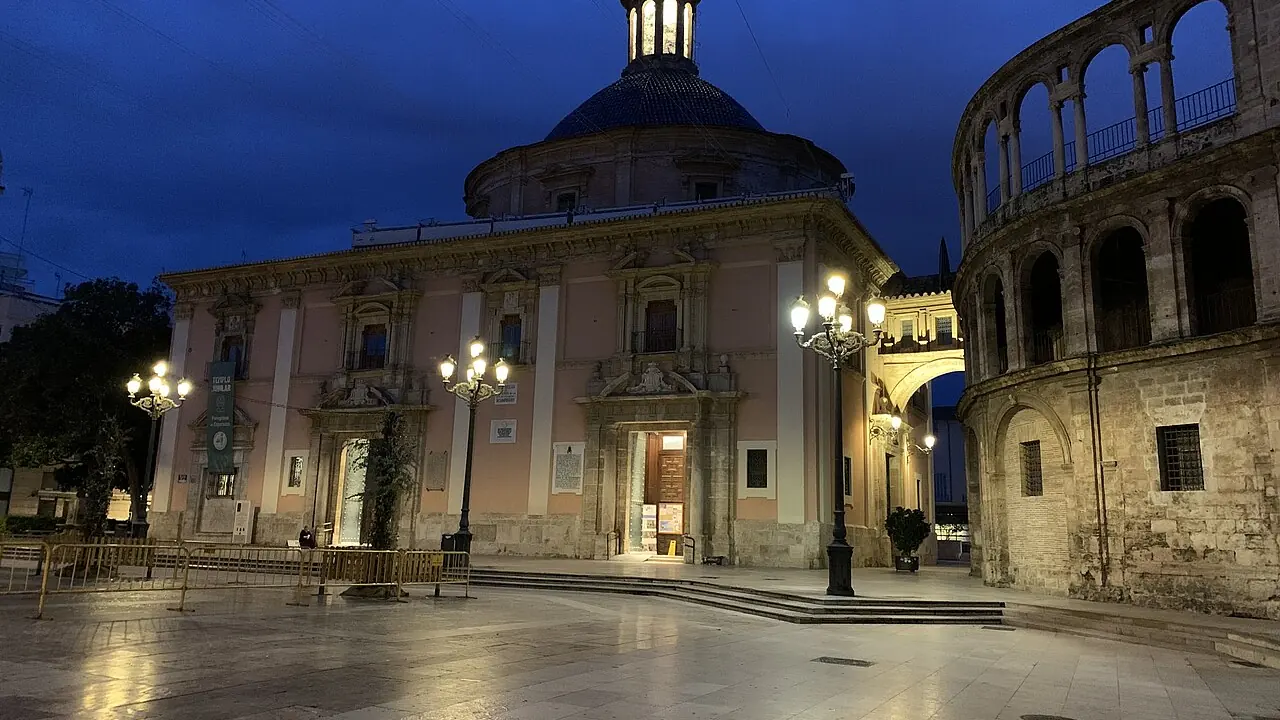 The Plaça de la Mare de Déu in Valencia at dawn with the basilica lit by street lamps and the square still empty