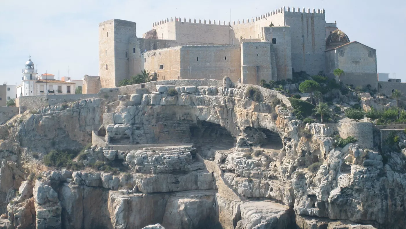 Le château de Peñíscola vu depuis la mer, forteresse de pierre claire aux tours crénelées sur un promontoire rocheux au-dessus d'une eau turquoise