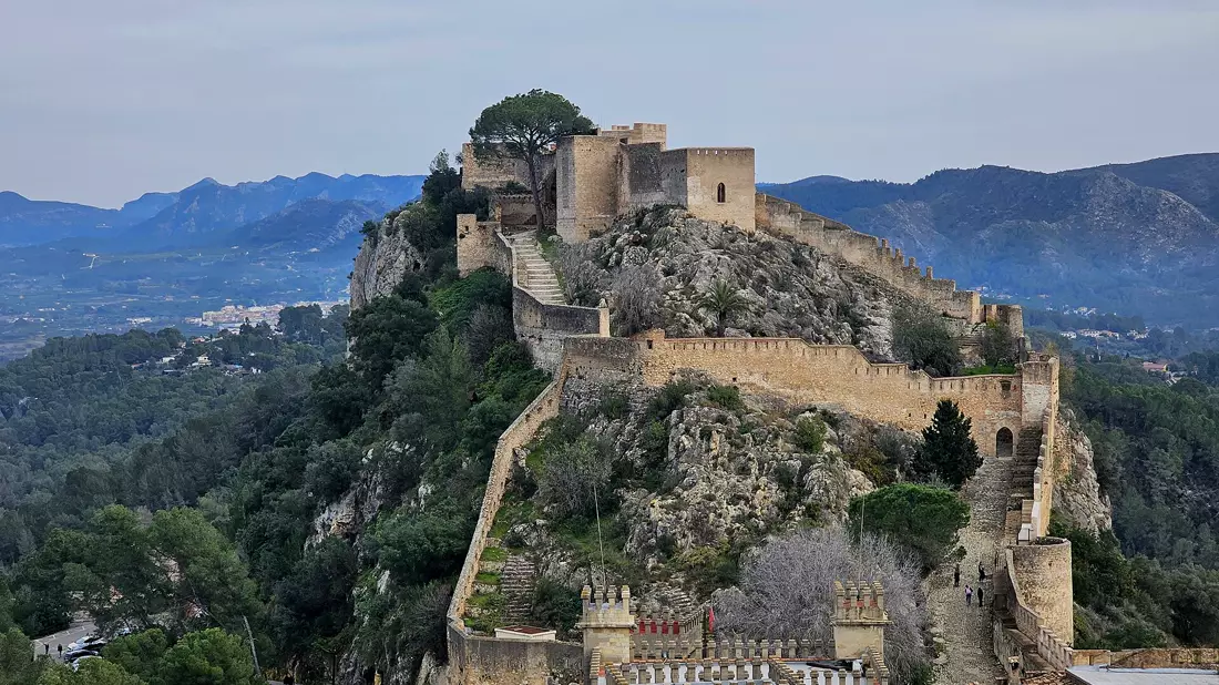 La crête du château de Xàtiva avec ses longs remparts crénelés et ses tours au-dessus de pinèdes, des montagnes en arrière-plan