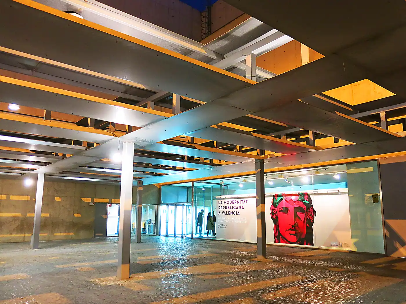Le portique d'entrée en béton du MuVIM à Valencia, avec une bâche d'exposition suspendue sous la galerie couverte