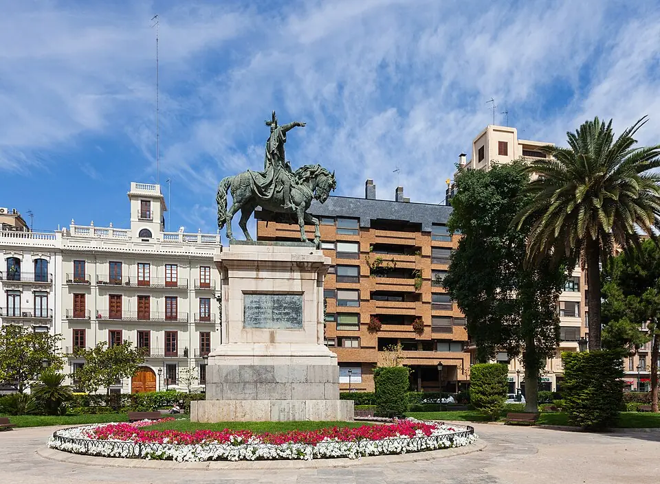 Bronzen ruiterstandbeeld van koning Jaume I op een stenen sokkel op een plein in Valencia, omringd door rode en witte bloemen