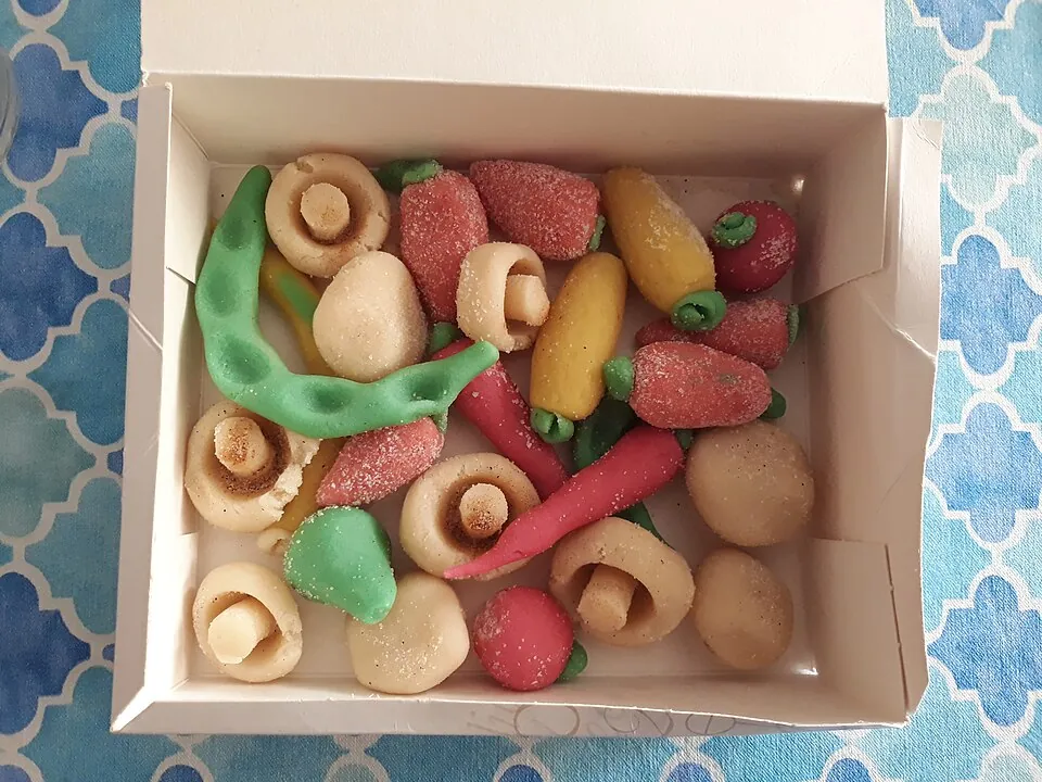 Open kartonnen doos met marsepein in de vorm van champignons, aardbeien, wortels en een erwtenpeul
