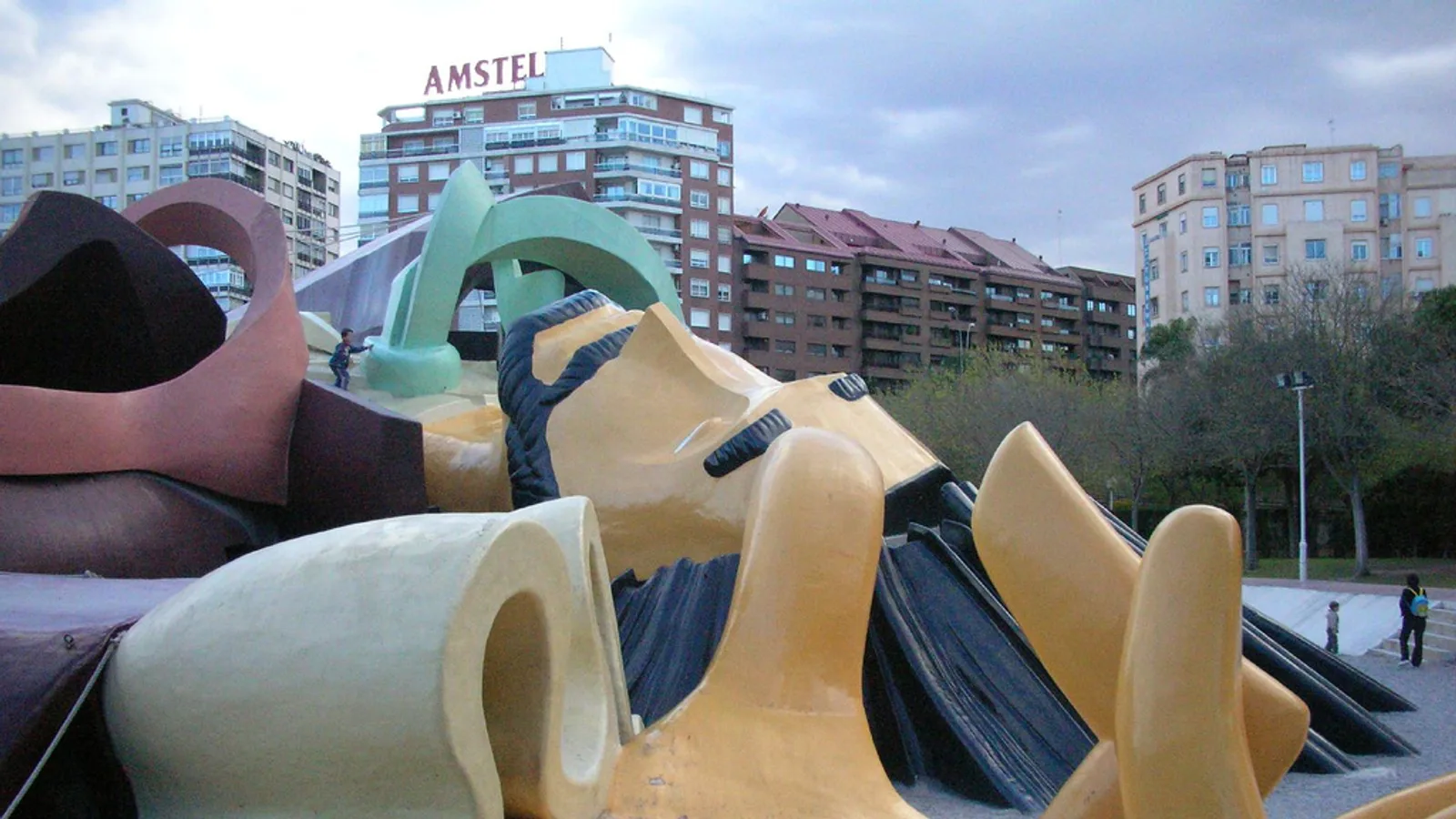 A giant reclining Gulliver sculpture used as a climbing playground, apartment buildings visible behind the park