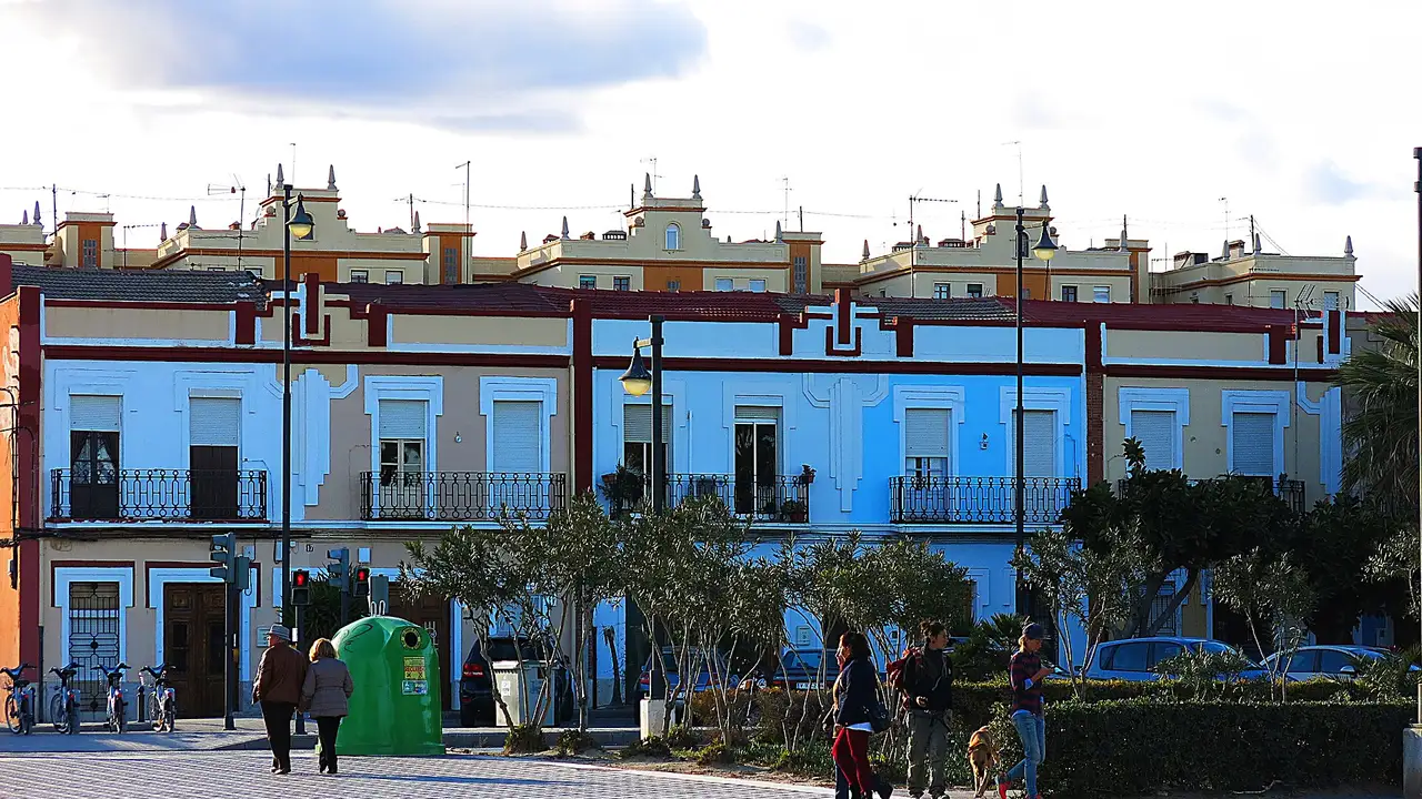 Una hilera de casas de dos plantas con fachadas pintadas y balcones de forja frente al paseo marítimo del Cabanyal