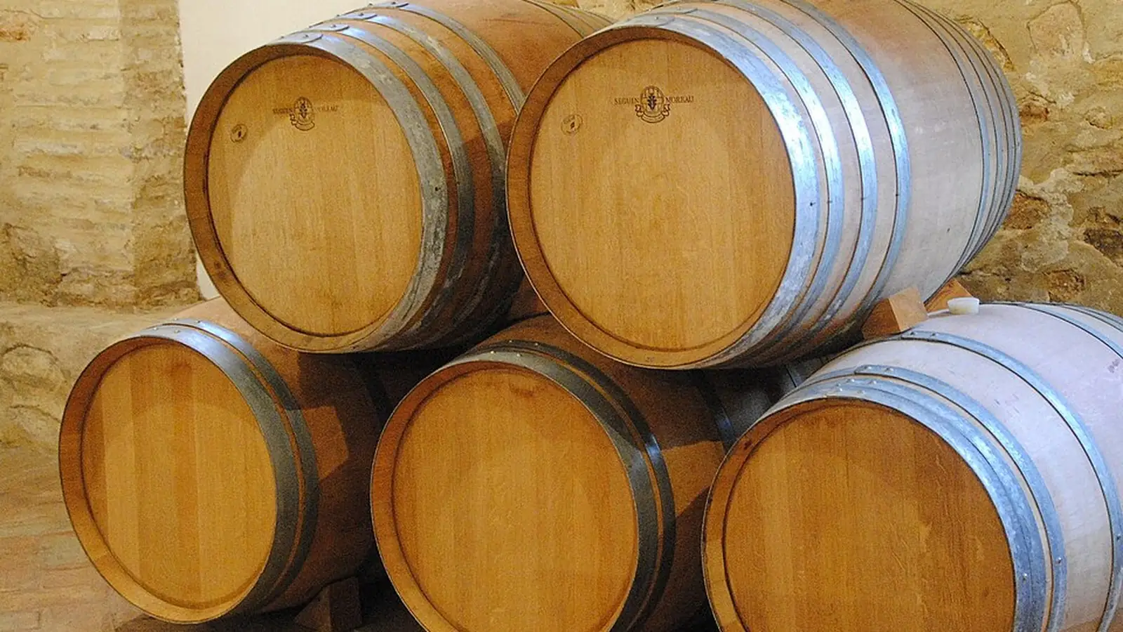 Oak barrels stacked against a rough stone wall in a winery cellar in Requena