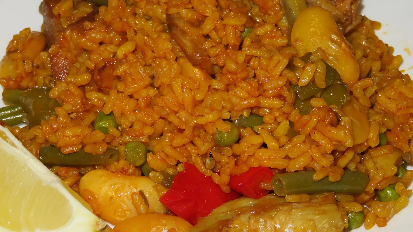 Una ración servida de paella valenciana con pollo, bajoqueta, garrofón y alcachofa, con un gajo de limón