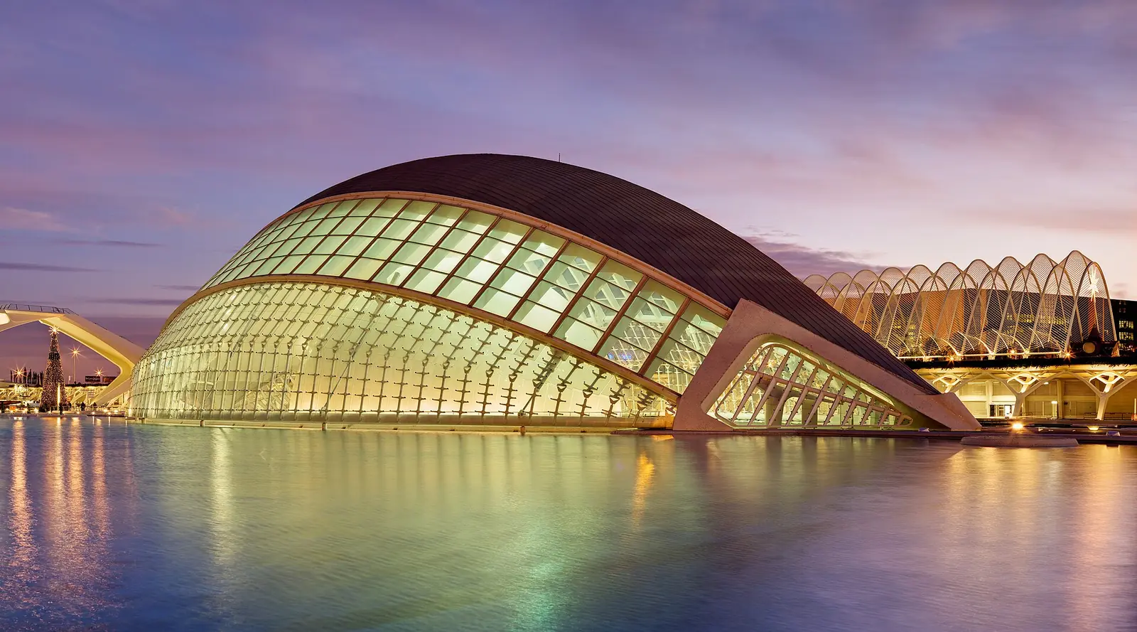 L'Hemisferic lit at dusk, its eye-shaped roof reflected in the pool of the City of Arts and Sciences
