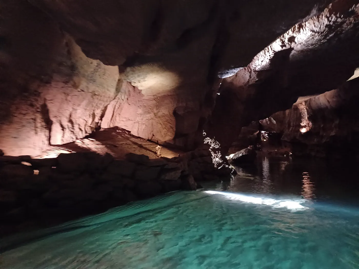 L'eau turquoise de la rivière souterraine traversant une salle rocheuse éclairée, à l'intérieur des Coves de Sant Josep