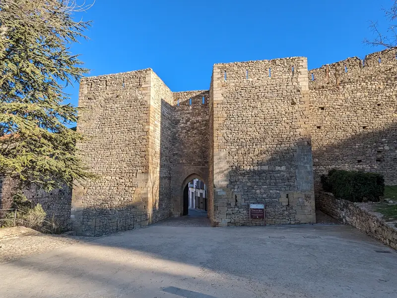 Une porte médiévale à deux tours dans les remparts de Morella, avec un passage en arc brisé et une rue blanchie visible au travers