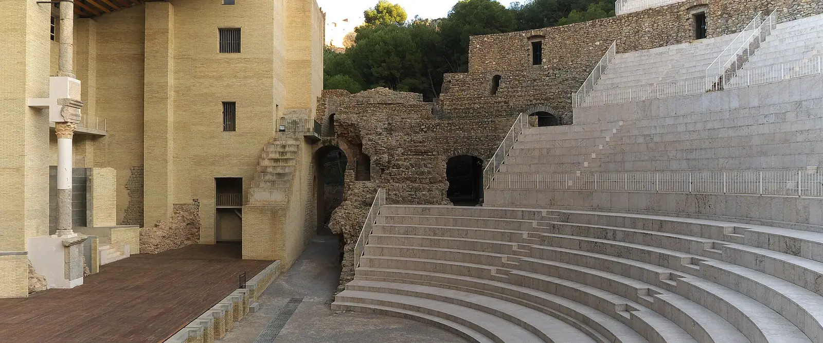 Les gradins et la scène du théâtre romain de Sagunto, avec les murs en pierre de la cavea et les pins de la colline en arrière-plan