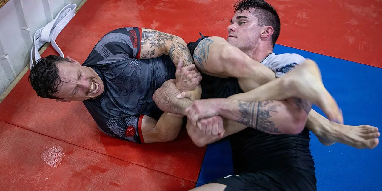 Twee mannen in een grondgevecht op rode en blauwe matten tijdens een Braziliaanse jiujitsutraining