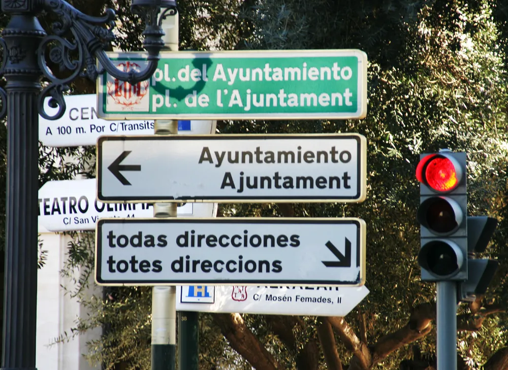 Des panneaux de direction en espagnol et en valencien près de la place de l'hôtel de ville, où l'on lit pl. del Ayuntamiento et pl. de l'Ajuntament, todas direcciones et totes direccions