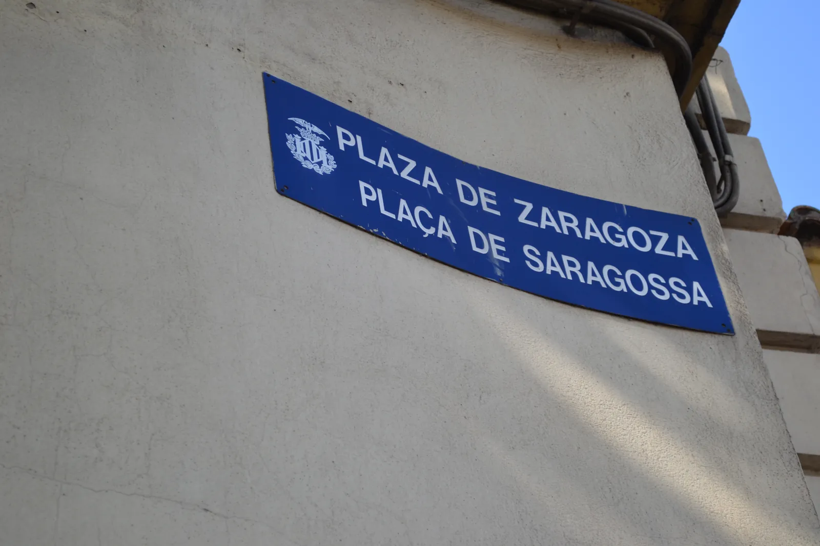 A blue street plate reading Plaza de Zaragoza above Plaça de Saragossa, the same name in Spanish and Valencian