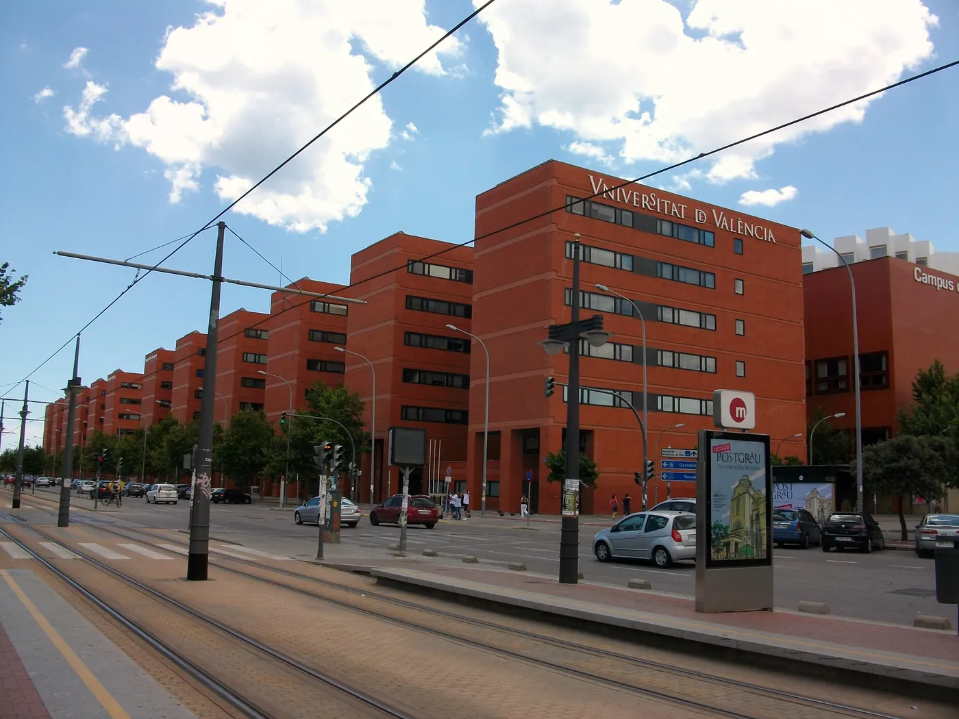 Red-brick Universitat de Valencia faculty buildings on the Tarongers campus, seen across the tram tracks from a Metrovalencia stop