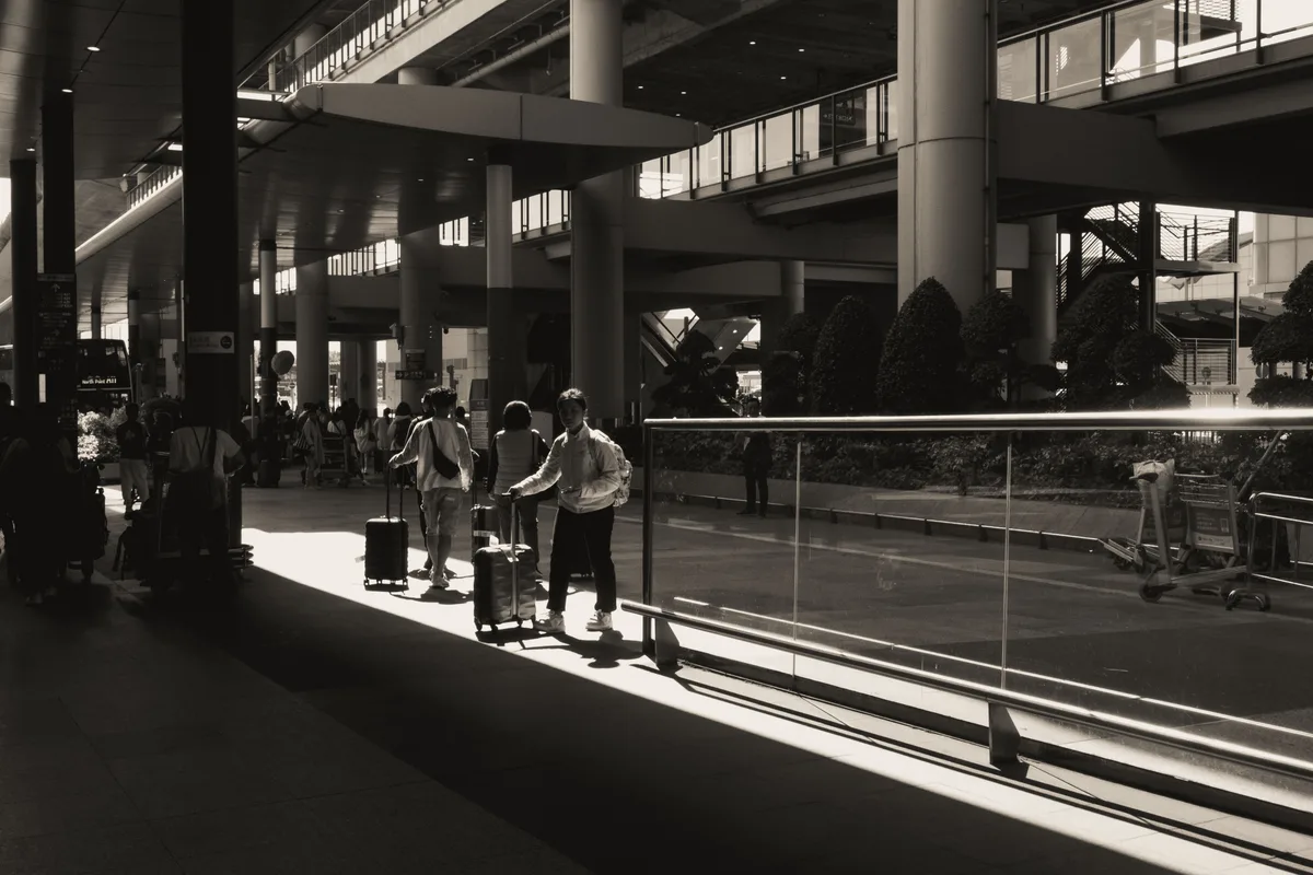 Viajeros en silueta con equipaje caminando por una terminal de aeropuerto iluminada por el sol