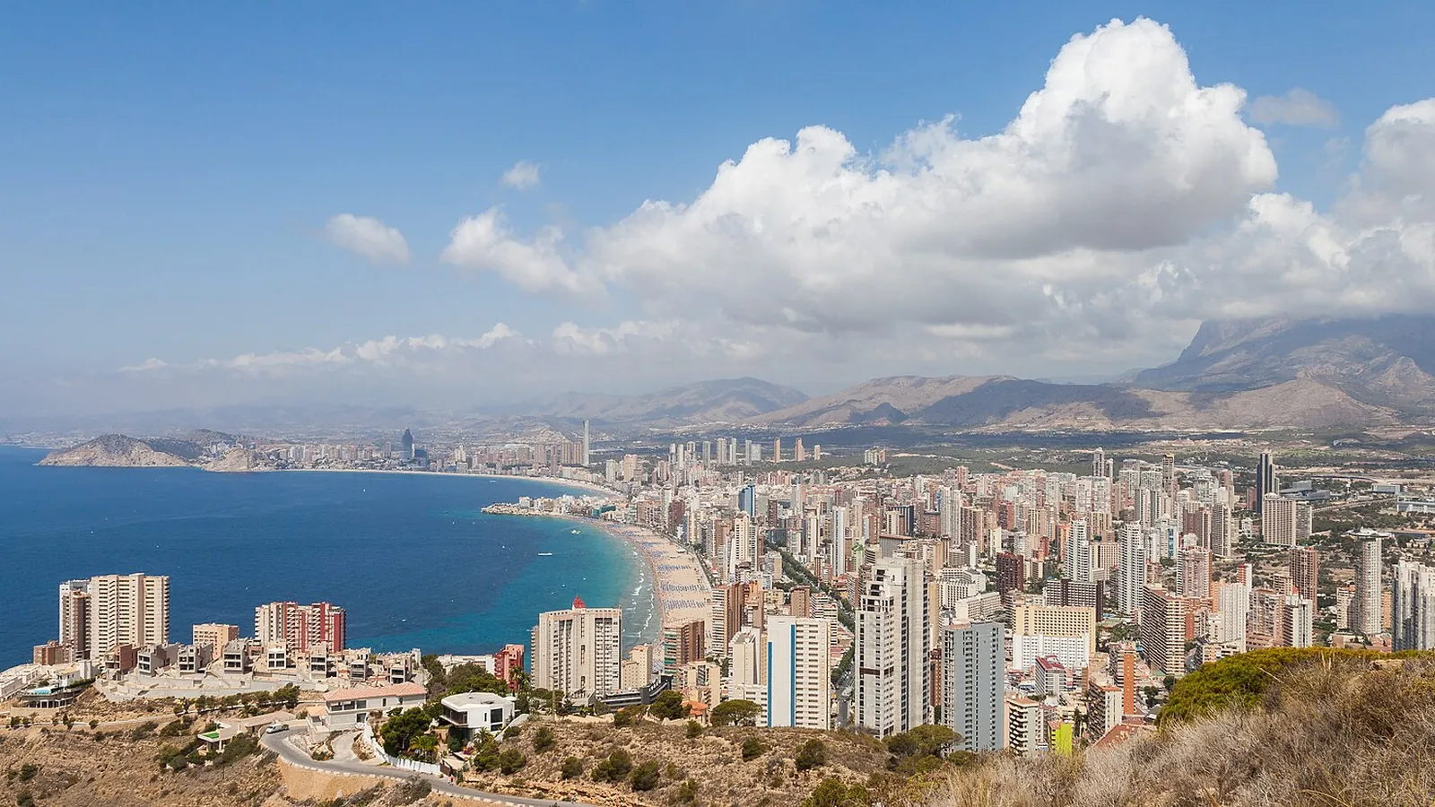 Benidorm vue depuis les collines au-dessus de la plage de Levante : la courbe de la plage, la ville et ses tours, et les montagnes derrière