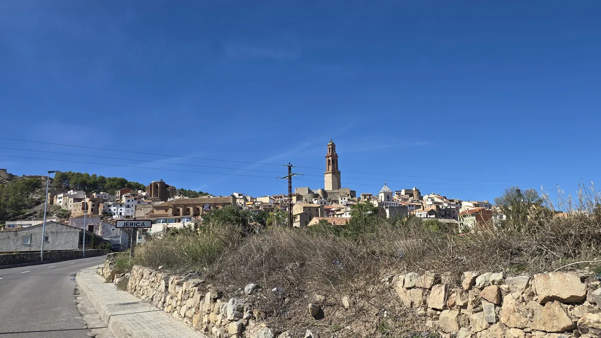 The road into Jérica with the town sign, the old town and its bell tower on the hill behind