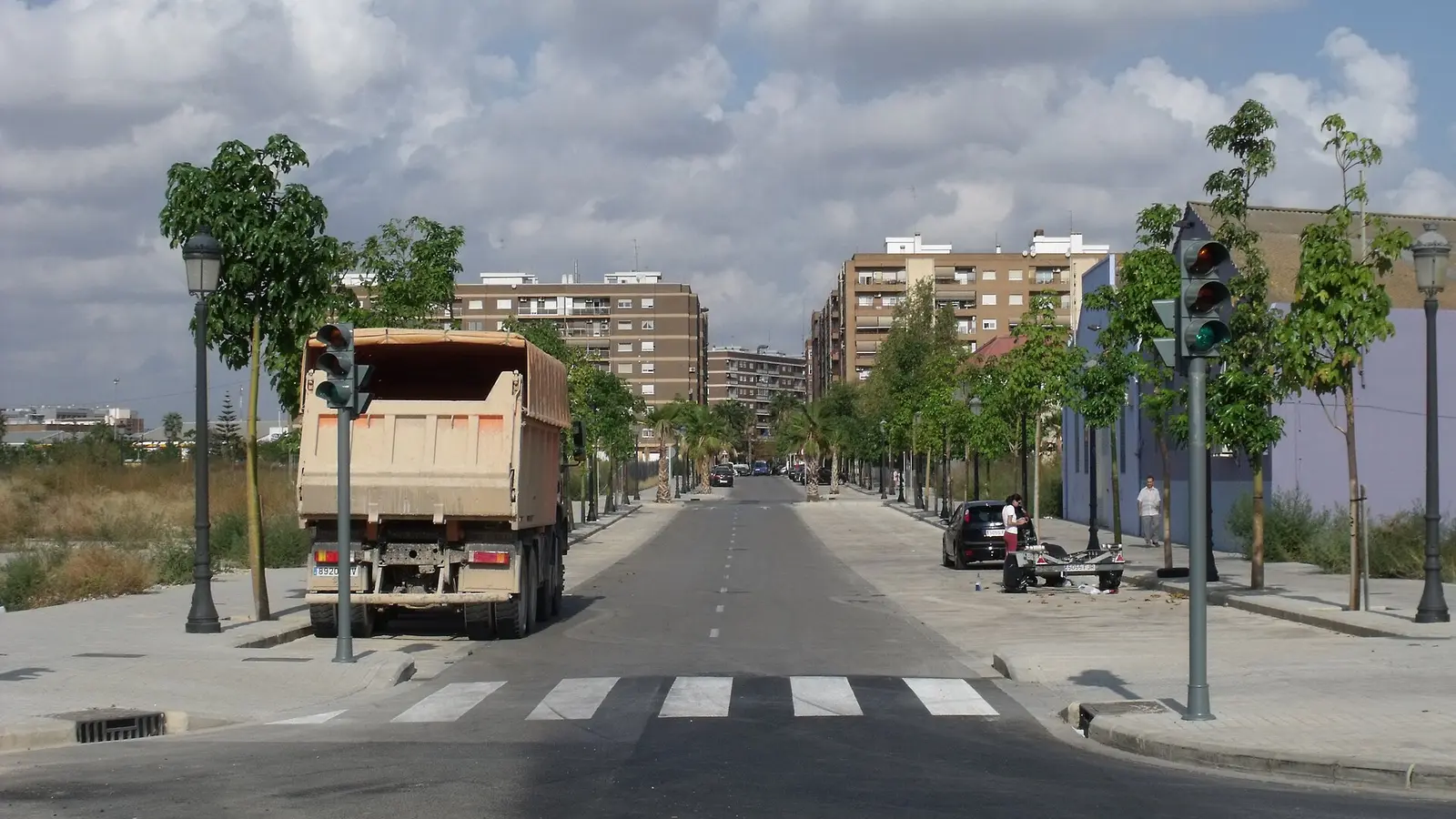 Une rue récente bordée d'arbres, avec feux de circulation et immeubles bruns des années 1970, Carrer de Campaners à Safranar, Valencia