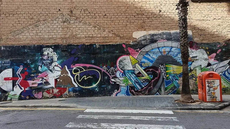 Une longue fresque de street art avec un astronaute et un aigle au pied d'un vieux mur de brique, Carrer d'Archena à Soternes, Valencia