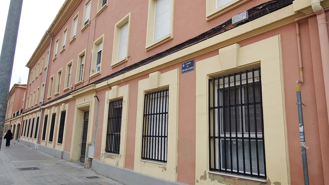 Un long immeuble résidentiel rose et crème de trois niveaux, aux fenêtres grillagées au rez-de-chaussée, Carrer de Santa Cruz de Tenerife à Tres Forques, Valencia