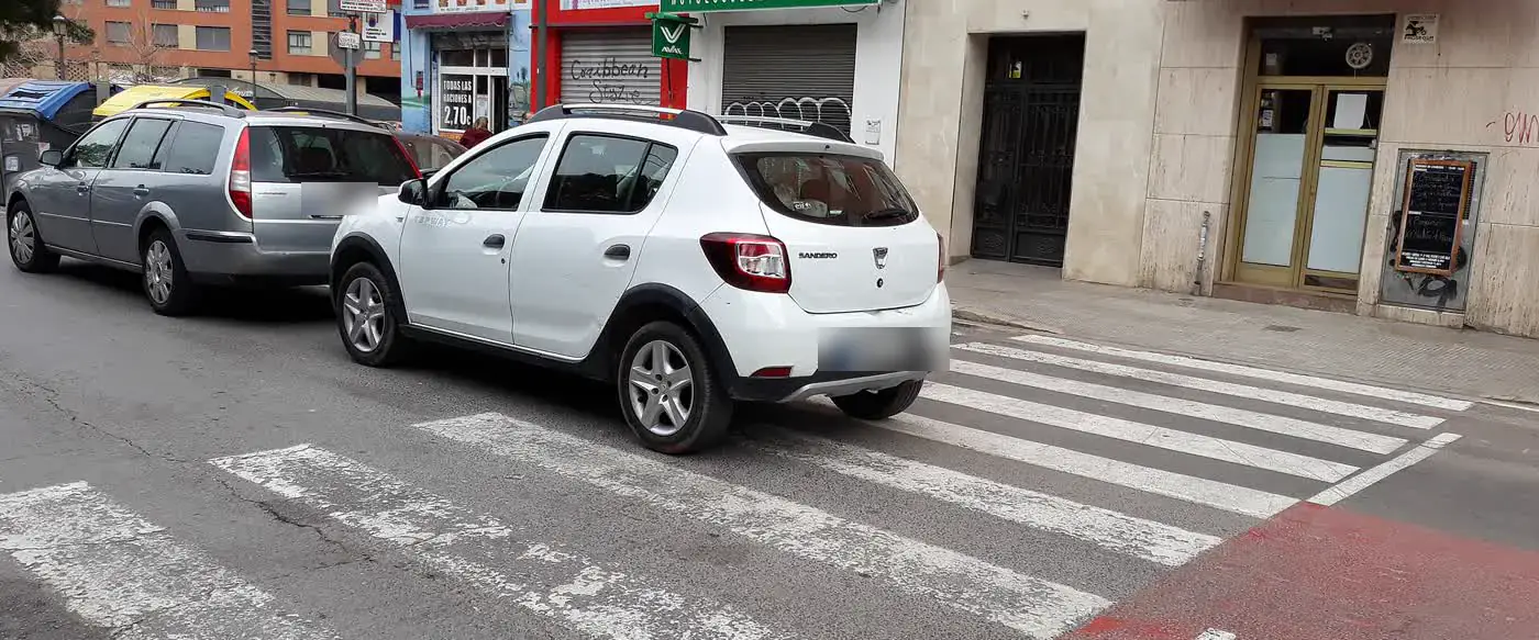 Un coche aparcado sobre un paso de cebra, junto a un carril bici rojo, en una calle de Valencia.