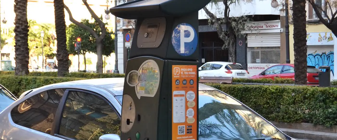 Un parquímetro verde de la ORA en la avinguda del Regne de València, con un coche aparcado en la plaza justo detrás.