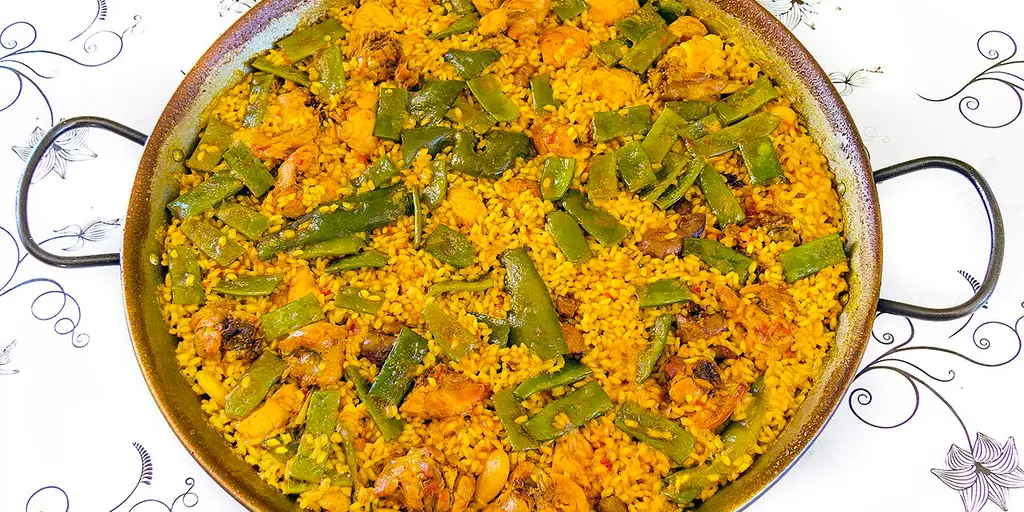 A paella valenciana in its shallow two-handled pan, golden rice with flat green beans and pieces of meat