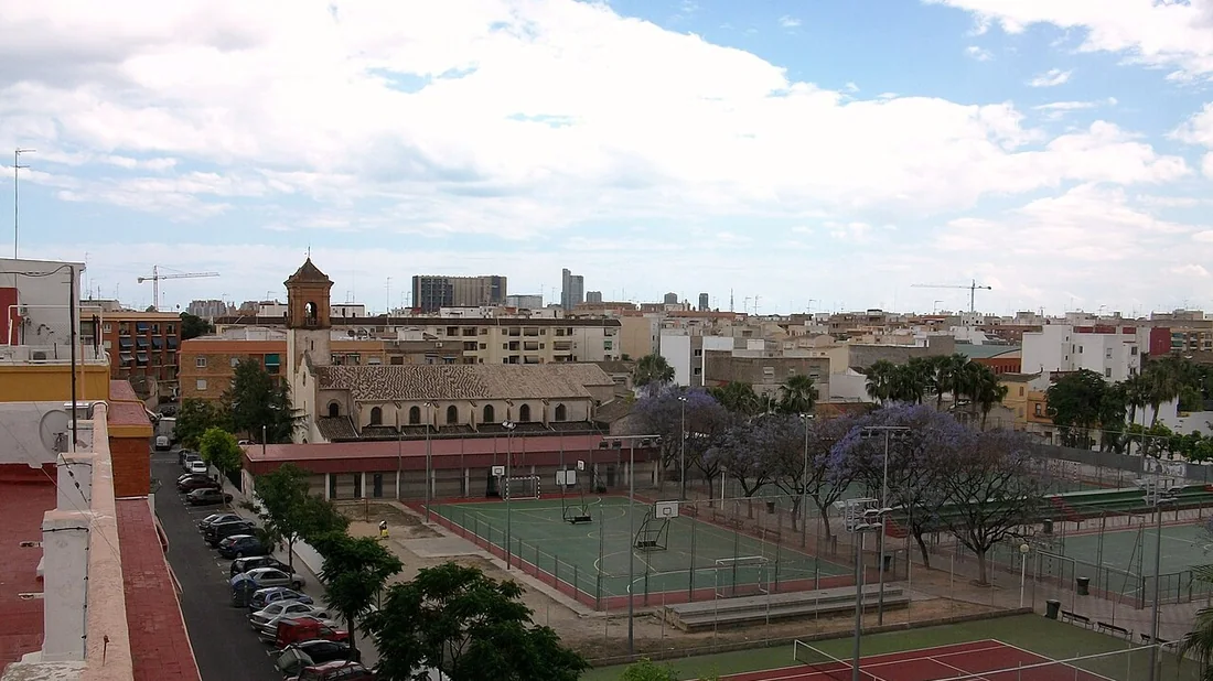 Vista desde una azotea de Burjassot con el campanario de la iglesia del Sagrat Cor, pistas deportivas y jacarandas delante del perfil de Valencia