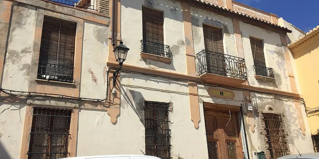 Older two-storey townhouses with iron balconies on a street in Naquera