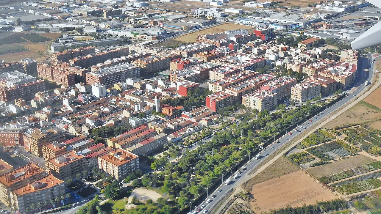 Vue aérienne de Xirivella, une ville dense d'immeubles en bordure d'un axe routier, avec des jardins maraîchers en lisière