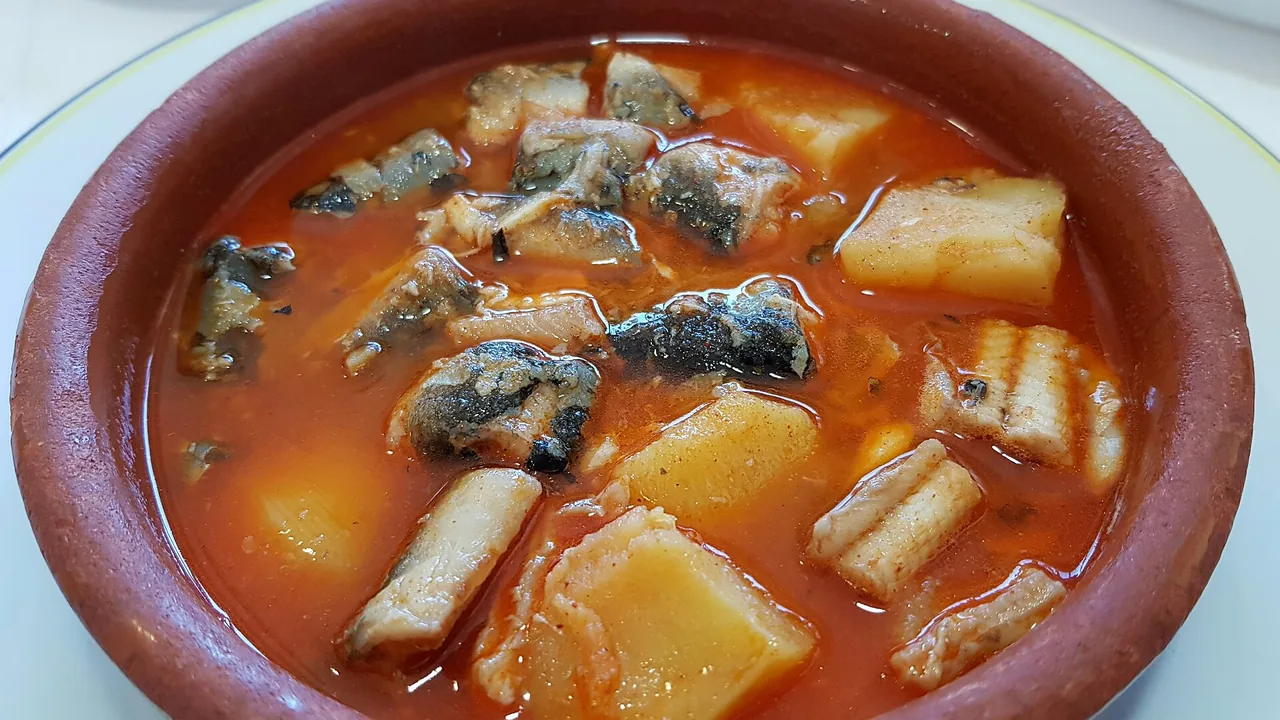 A clay dish of all i pebre: pieces of eel and potato in a red paprika broth